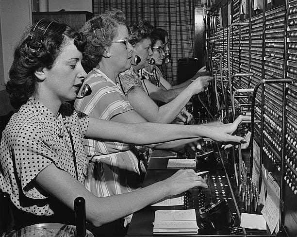 Ženy na telefónnej ústredni pracujúce na prepájaní hovorov v čiernobielom retro štýle.