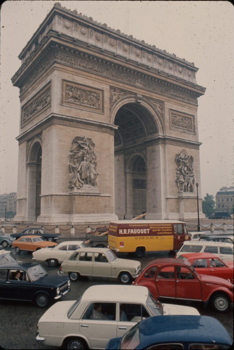 Víťazný oblúk v Paríži obklopený premávkou na rušnej križovatke, historická pamiatka s autami v popredí.