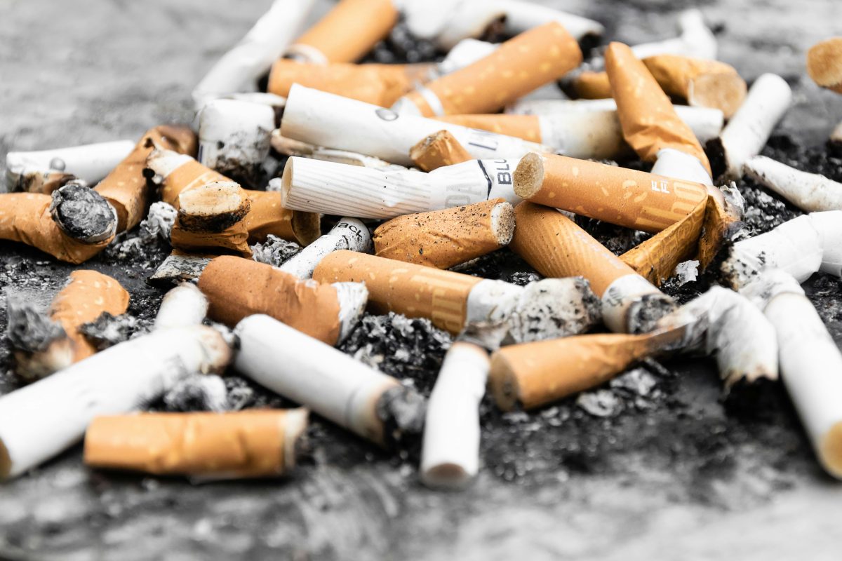 Použité cigaretové ohorky na zemi, symbol znečistenia a environmentálnej záťaže fajčenia.