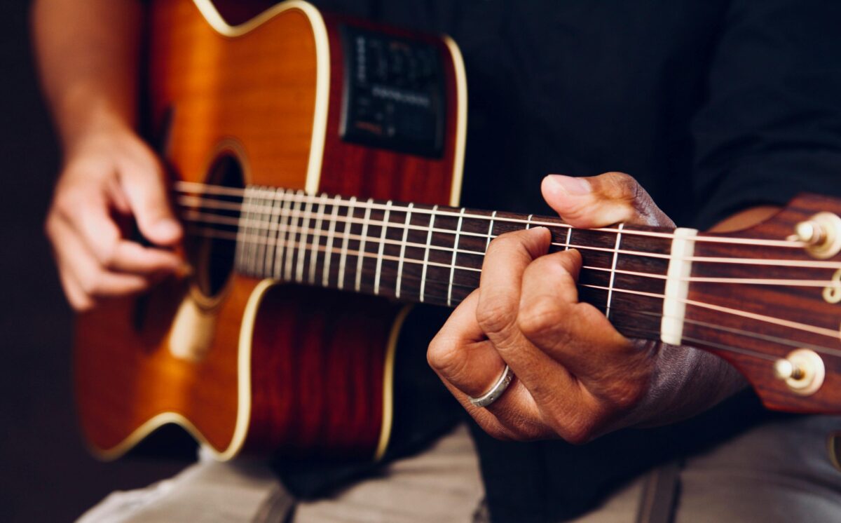 Osoba hrá na akustickej gitare, detail strún a prstov.