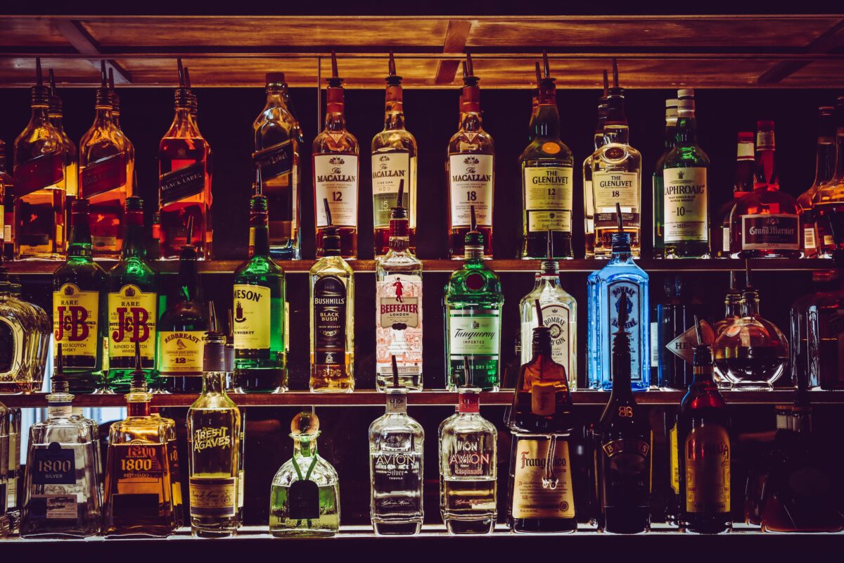 Rôzne fľaše alkoholu vystavené na poličke v bare, vrátane whisky, ginu a ďalších nápojov.