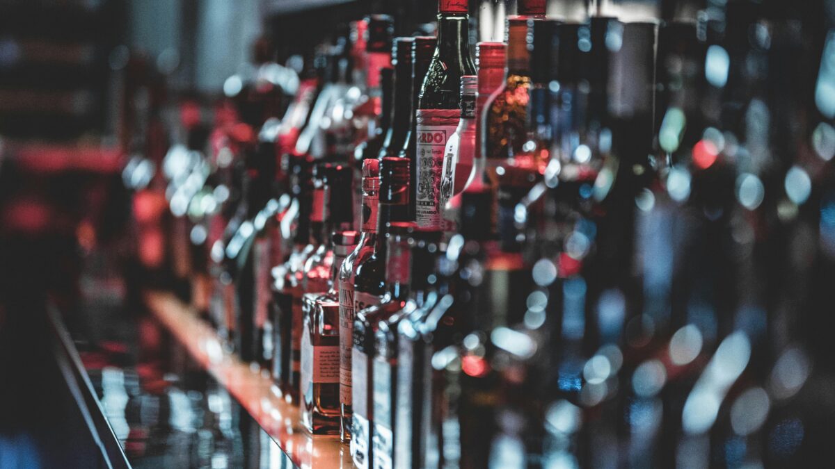 Fľaše alkoholu usporiadané na policiach v tmavom bare.