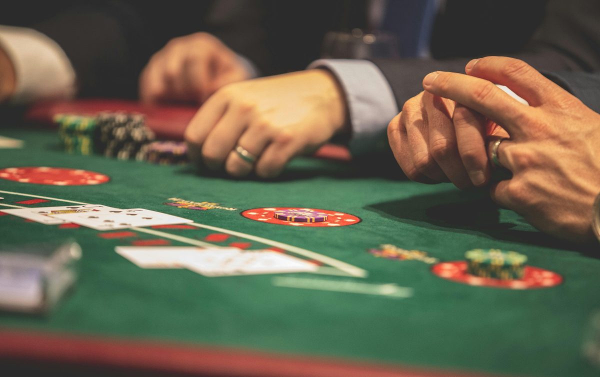 Ľudia hrajúci poker pri stole v kasíne, s kartami a žetónmi na zelenom plátne.