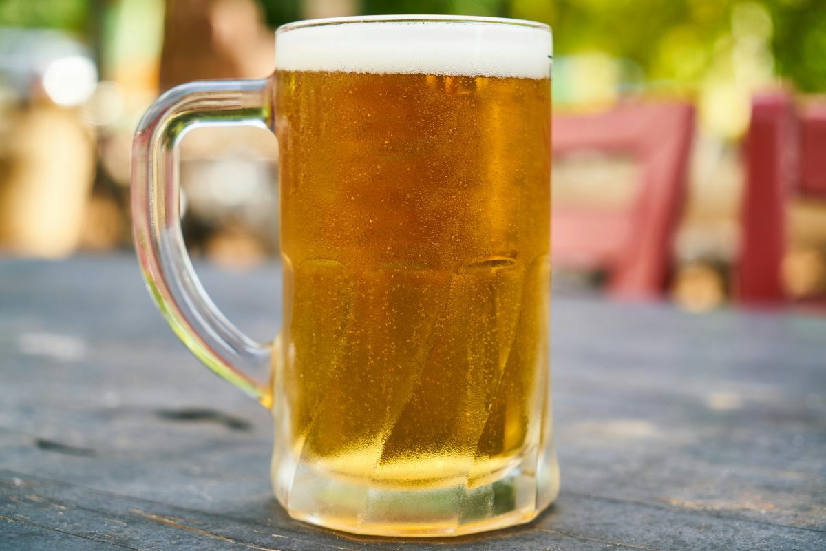 Pohár zlatistého piva na drevenom stole v príjemnom vonkajšom prostredí.