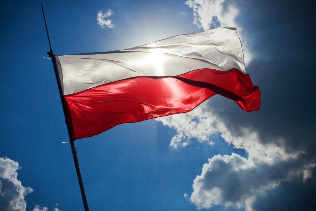 Poľská vlajka vlajúca vo vetre na modrom pozadí oblohy so slnečnými lúčmi.