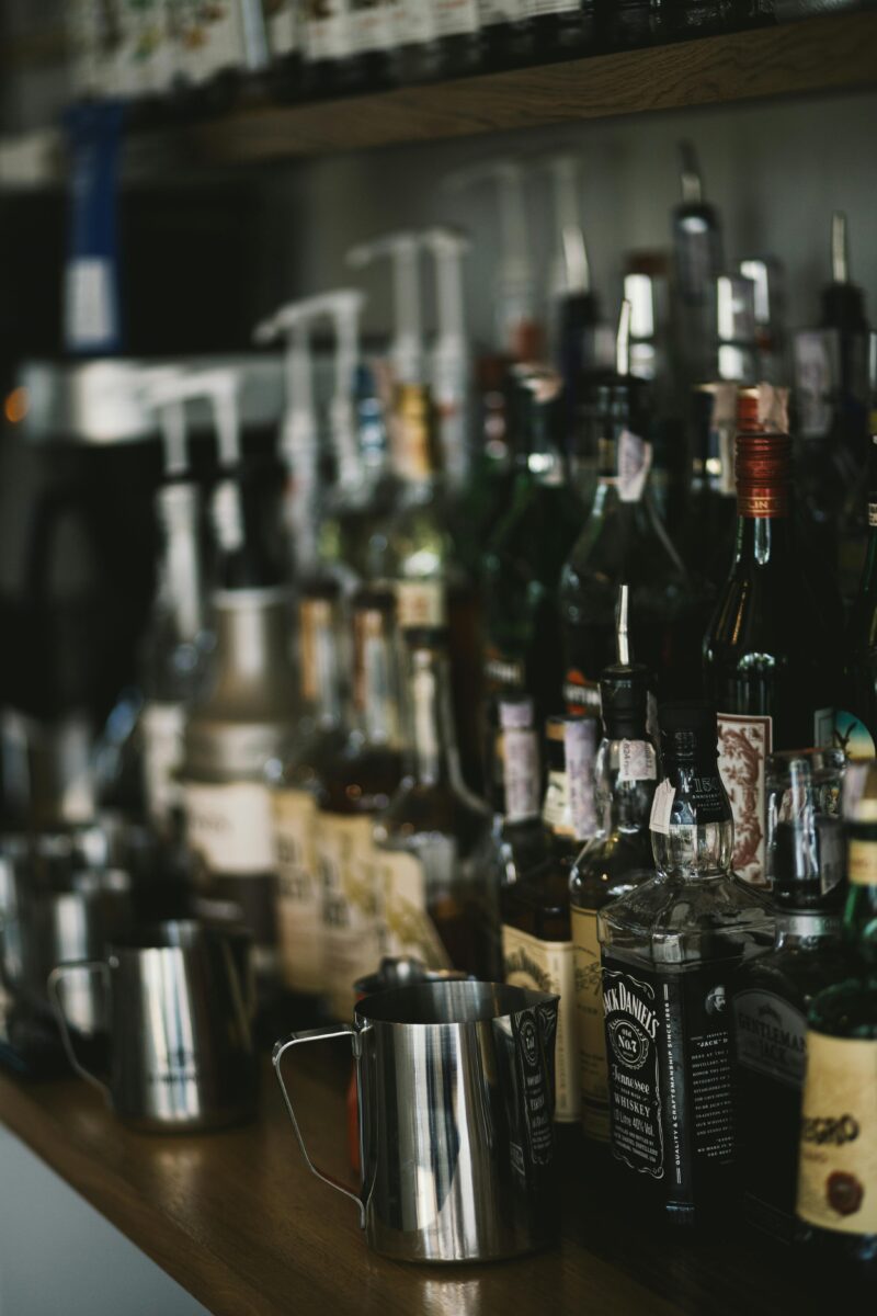 Polička s rôznymi fľašami alkoholu a nerezovými džbánmi v bare.
