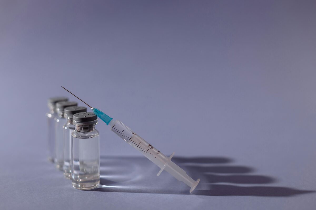 Injekčná striekačka a fľaštičky na lieky na fialovom pozadí, koncept očkovania alebo medicíny.