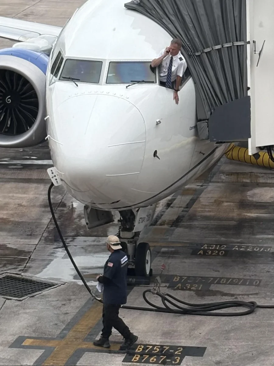 Pilot telefonuje z okna kokpitu lietadla počas prípravy na let na letisku.