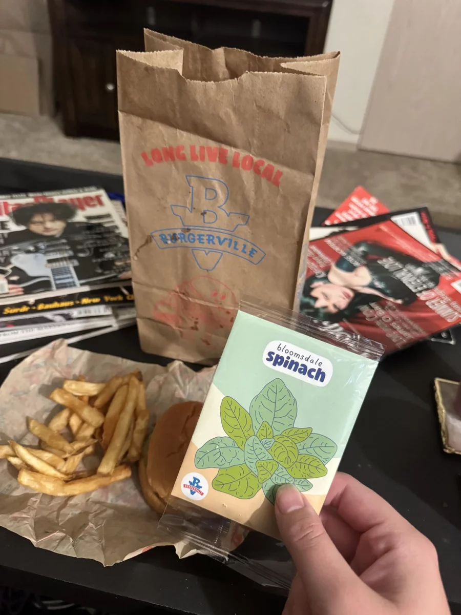Fast food jedlo Burgerville s hranolkami a hamburgerom, vedľa semienok špenátu Bloomsdale na stole s časopismi.