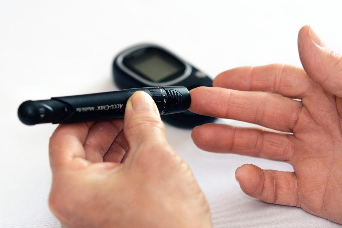 Osoba používa glukometer na meranie hladiny cukru v krvi na bielom pozadí.