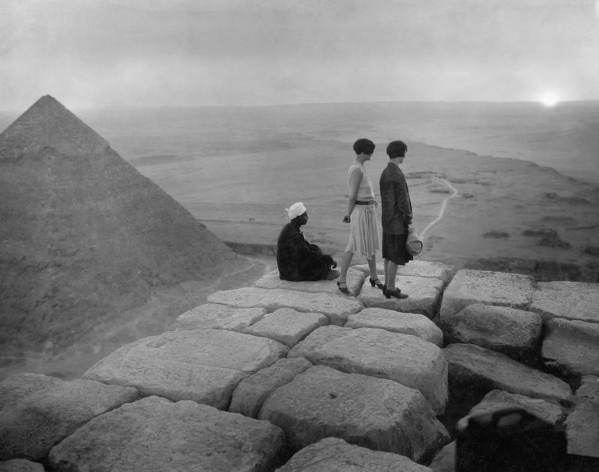 Ľudia na vrchole pyramídy pozorujú západ slnka nad púšťou v Gíze.