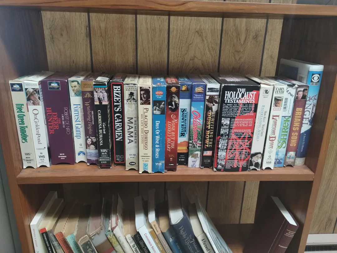 Polica s VHS kazetami rôznych filmov a dokumentov v drevenej skrini.