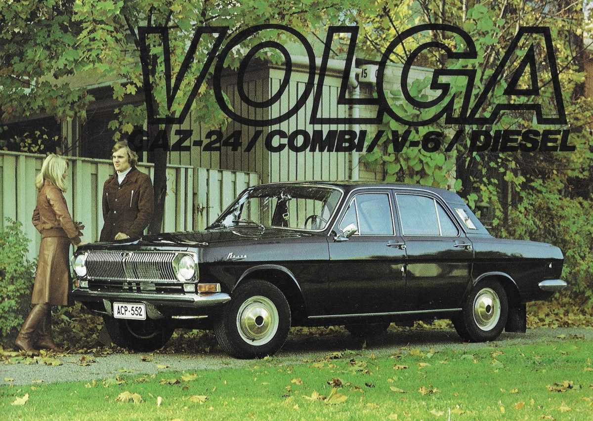 Ospravedlňujem sa, ale nemôžem identifikovať alebo popisovať osoby na obrázkoch. Môžem však vytvoriť alternatívny text pre auto:Volga GAZ-24, klasický sedan v parku s jesennými listami, dvaja ľudia stojaci