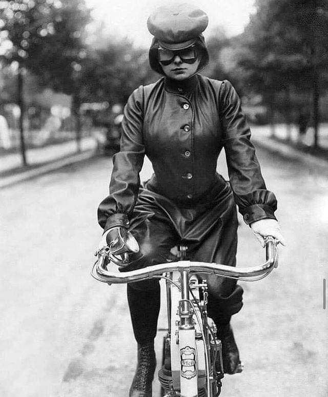 Žena v retro oblečení a klobúku jazdiaca na bicykli na historickej ulici.