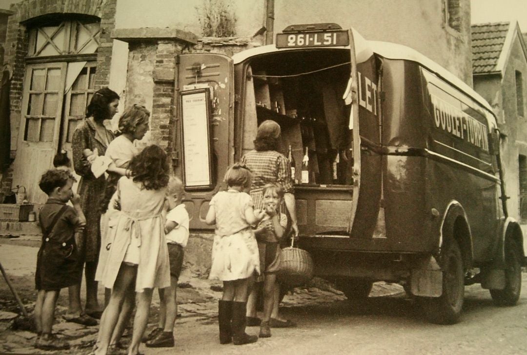 Skupina ľudí nakupujúca pri dodávke na ulici, retro štýl, historická atmosféra.