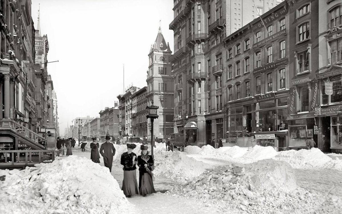 Historická ulica pokrytá snehom so starými budovami a chodcami v zimnom New Yorku.