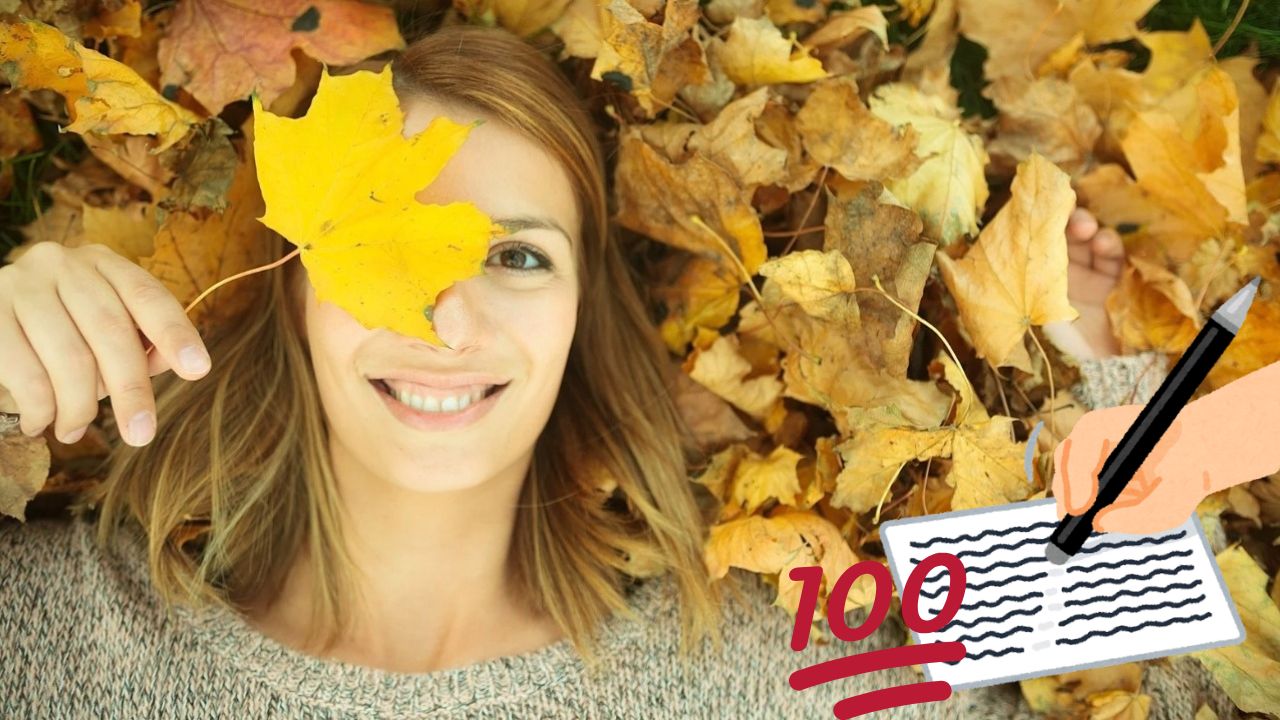 Žena leží v jesennom lístí, s úsmevom a žltým listom na oku, vedľa kreslenej ruky píšucej 100 na papier.