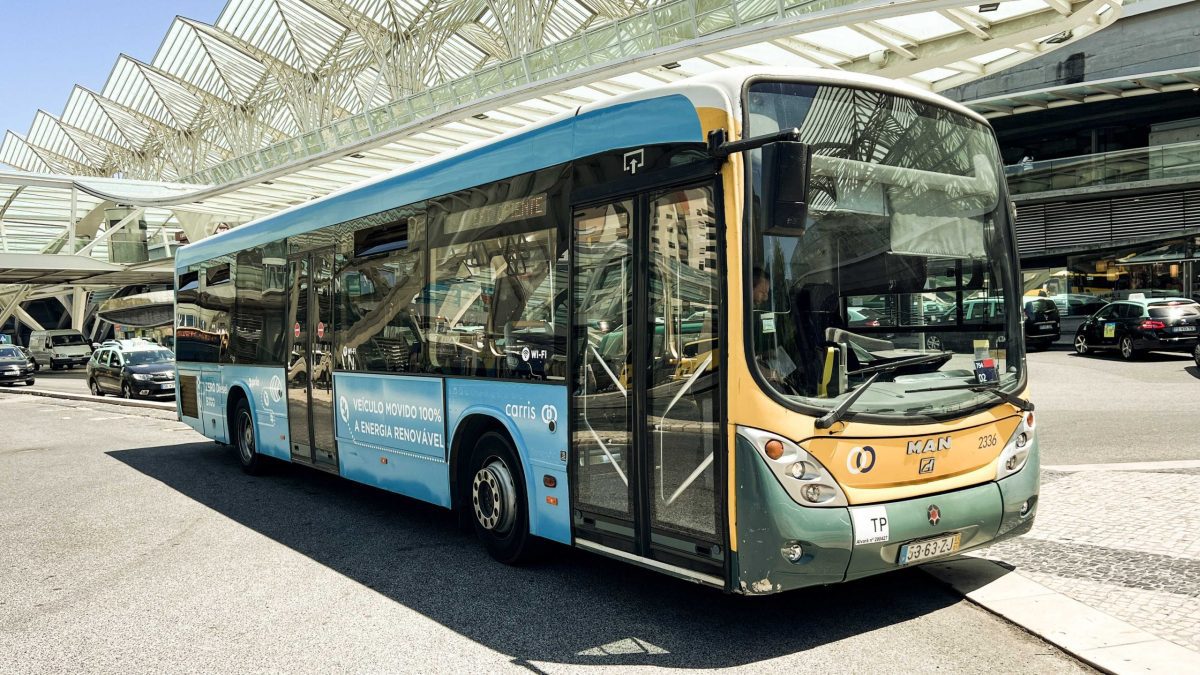 Modrý mestský autobus poháňaný obnoviteľnou energiou na rušnej ulici pred modernou stanicou za slnečného dňa.