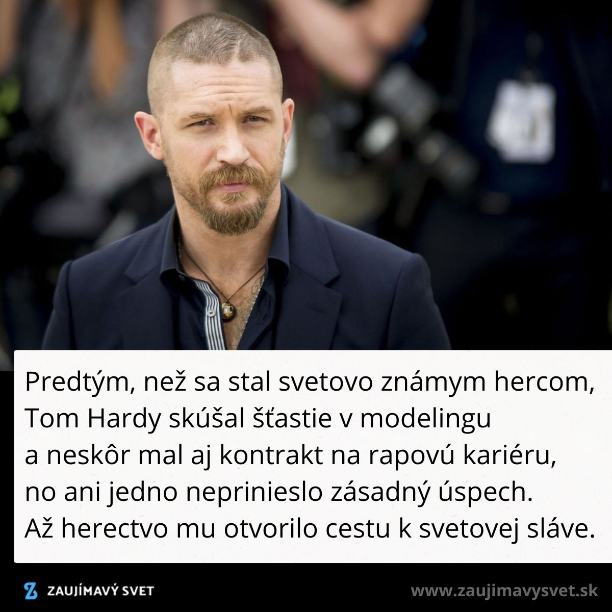 Herec v tmavom obleku na červenom koberci, kamera a dav v pozadí.
