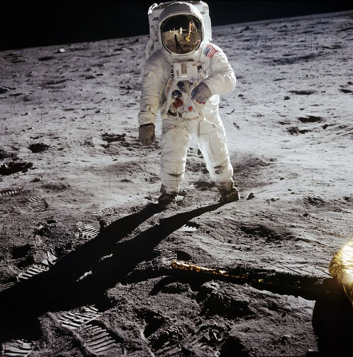 Astronaut v skafandri kráča po povrchu Mesiaca, obklopený lunárnym prachom a stopami svojich krokov.