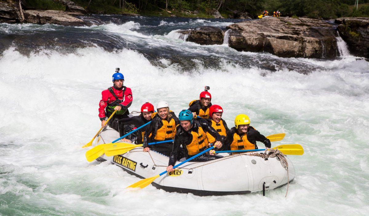 Skupina ľudí zažíva vzrušujúci rafting na divokej rieke, obklopení penivou vodou a hornatou prírodou.