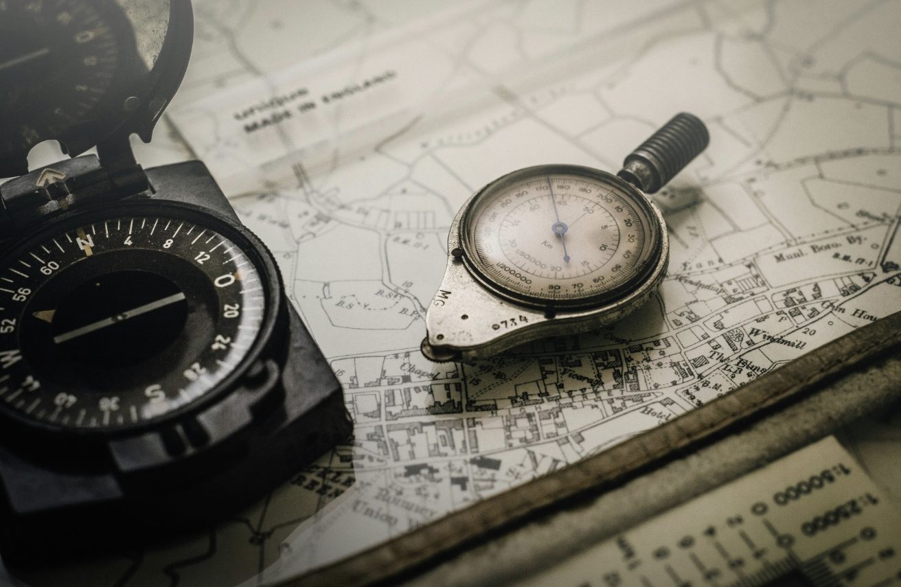 Starý kompas a výškomer položené na starodávnej mape, symbolizujúce navigáciu a prieskum.
