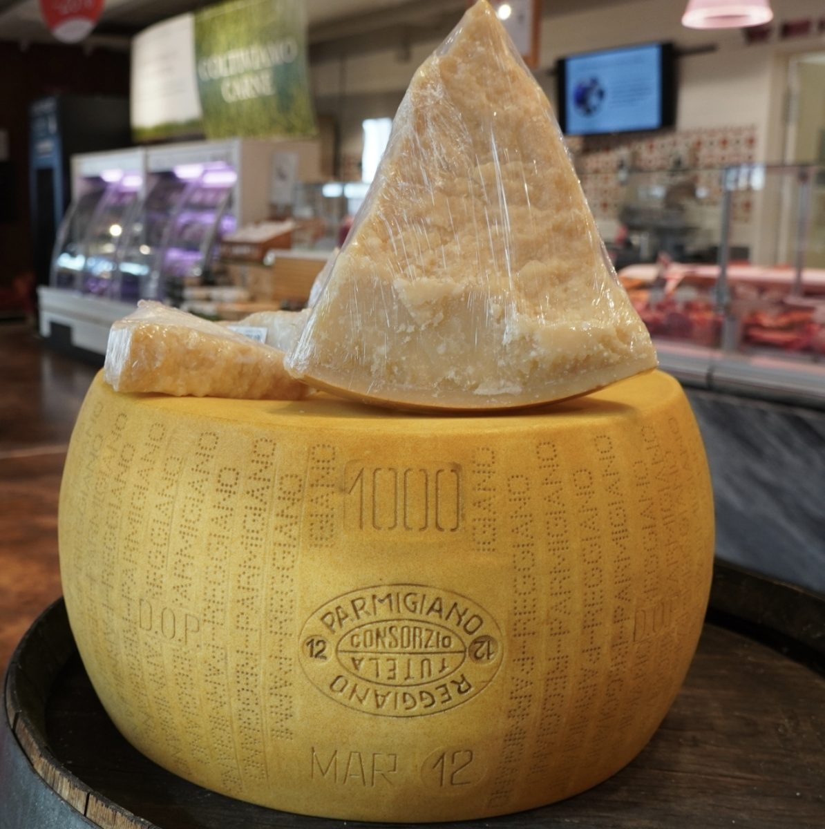 Kolo syra Parmigiano Reggiano so vzorkou na pulte v obchode s delikatesami.
