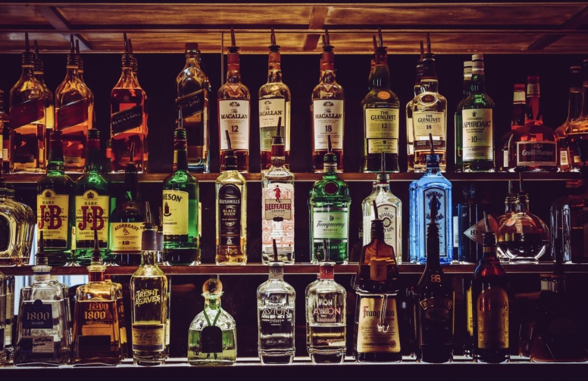 Rôzne druhy fliaš alkoholu vystavené na polici v bare s dreveným obložením.