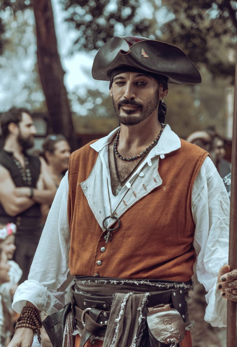 Muž oblečený ako pirát s trojrohým klobúkom na historickom festivale, v pozadí ďalší účastníci.