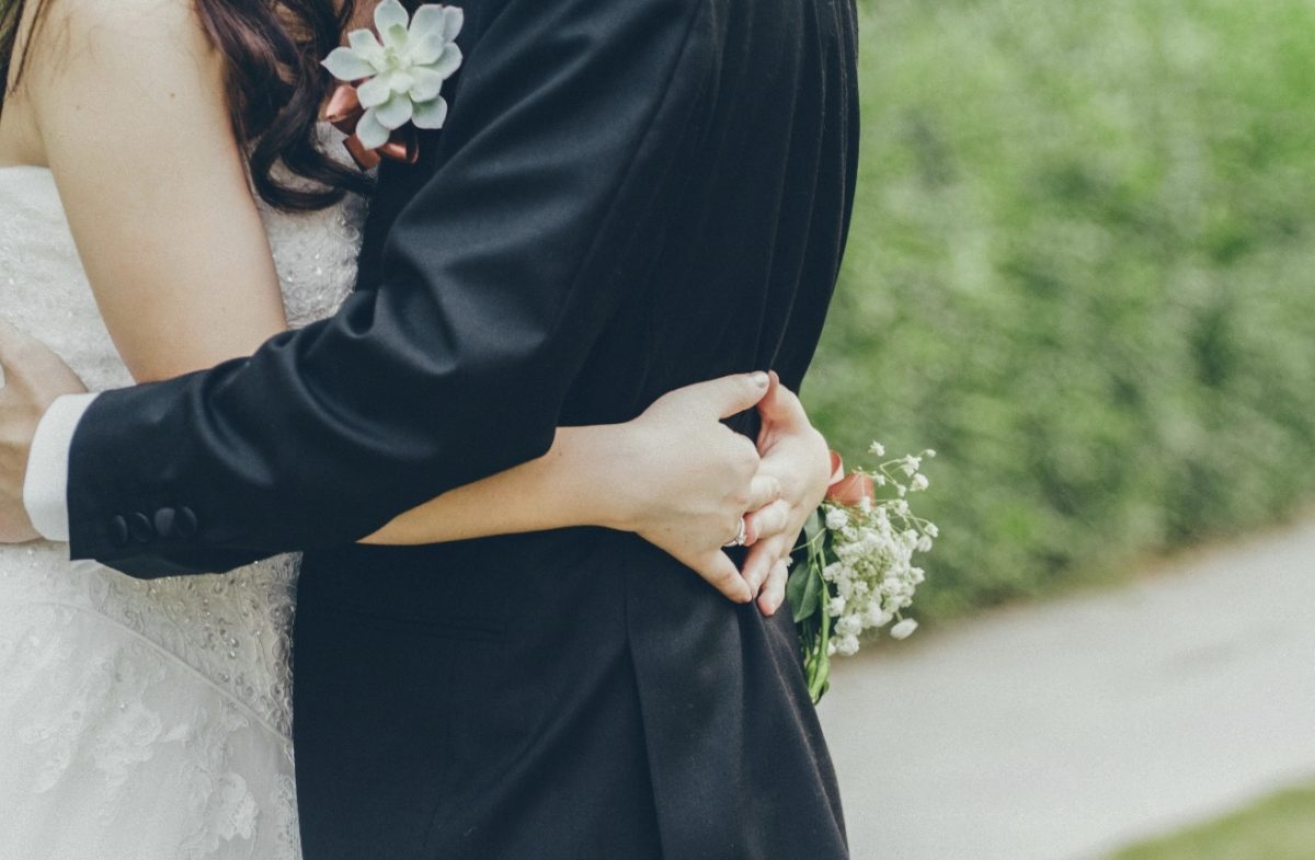 Nevesta a ženích sa objímajú na svadobnom obrade v prírode, detail ruky a kytice.