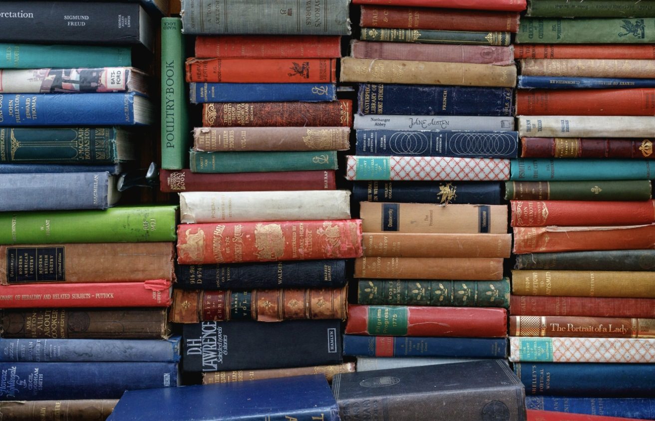 Rôznofarebné staré knihy poukladané v stohu na sebe, tvoriace vzor na pozadí plnom literárnej rozmanitosti.