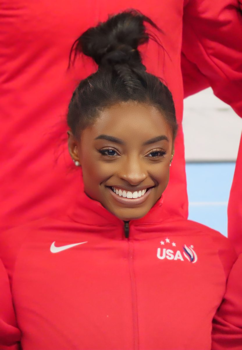 Osoba v červenej uniforme s logom USA sa usmieva, pozadie je rozmazané.