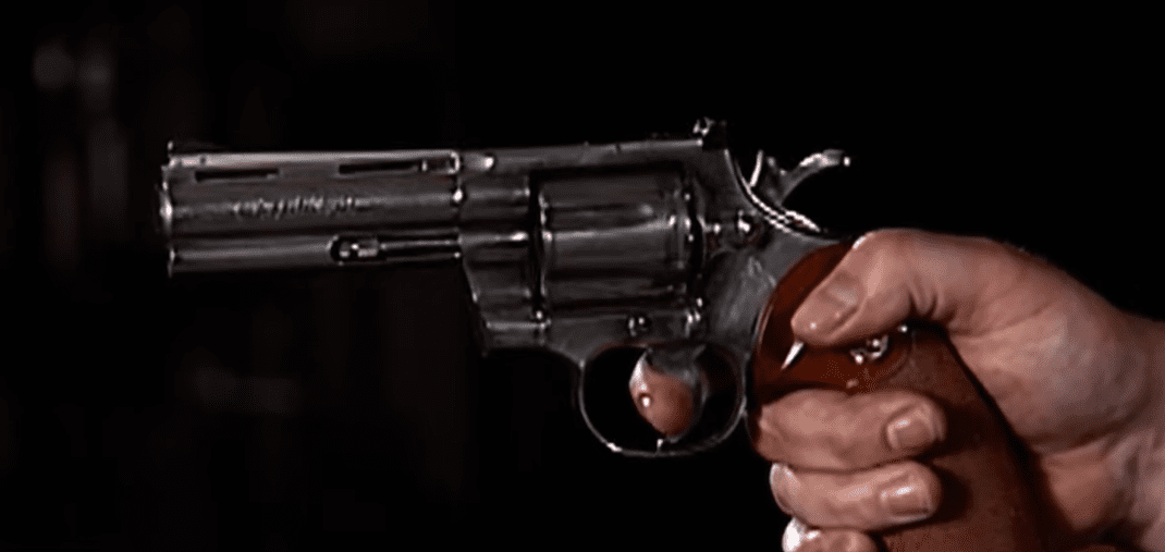 Revolver s drevenou rukoväťou namierený vodorovne zblízka proti tmavému pozadiu.