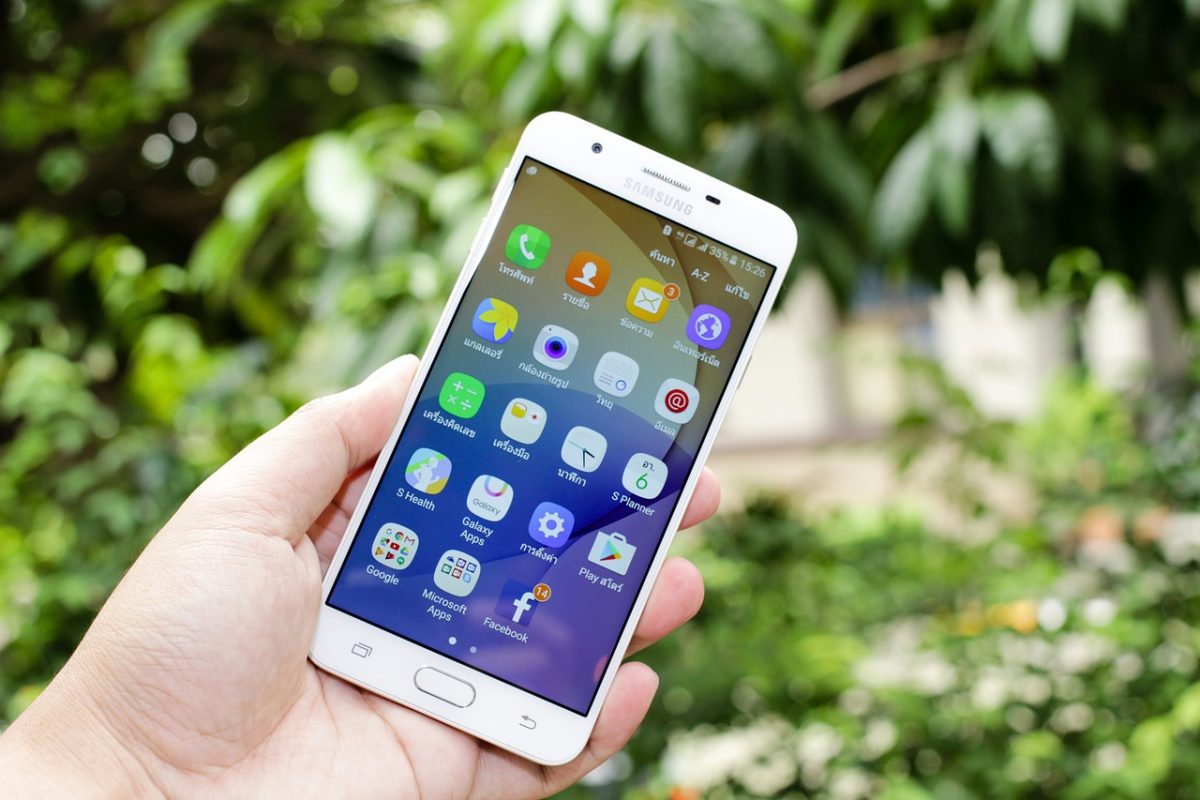 Osoba držiaca smartfón Samsung s otvorenou obrazovkou aplikácií v prírodnom prostredí.