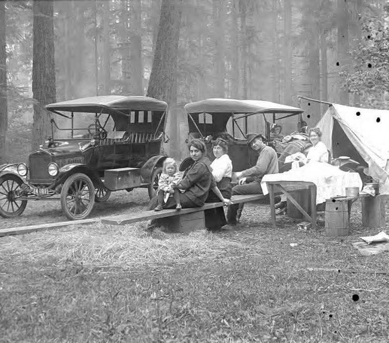 Rodina kempingujúc v lese s historickými automobilmi a pláteným stanom. Oddych na čerstvom vzduchu v prírode.