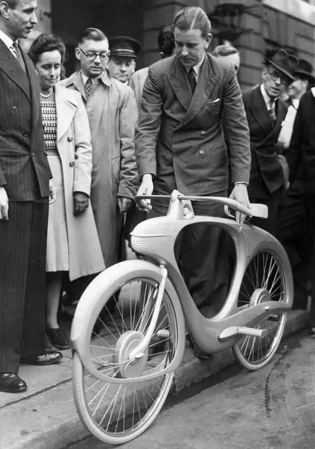 Muž skúma futuristický prototyp bicykla na verejnej výstave obklopený zvedavým davom ľudí.