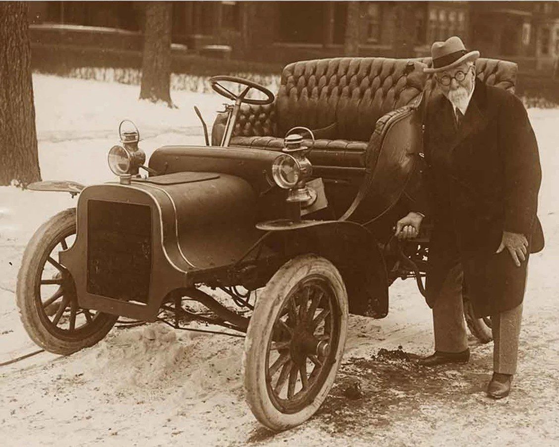 Starý pán pri historickom aute v zasneženom prostredí, zimná scéna s vintage kabrioletom.