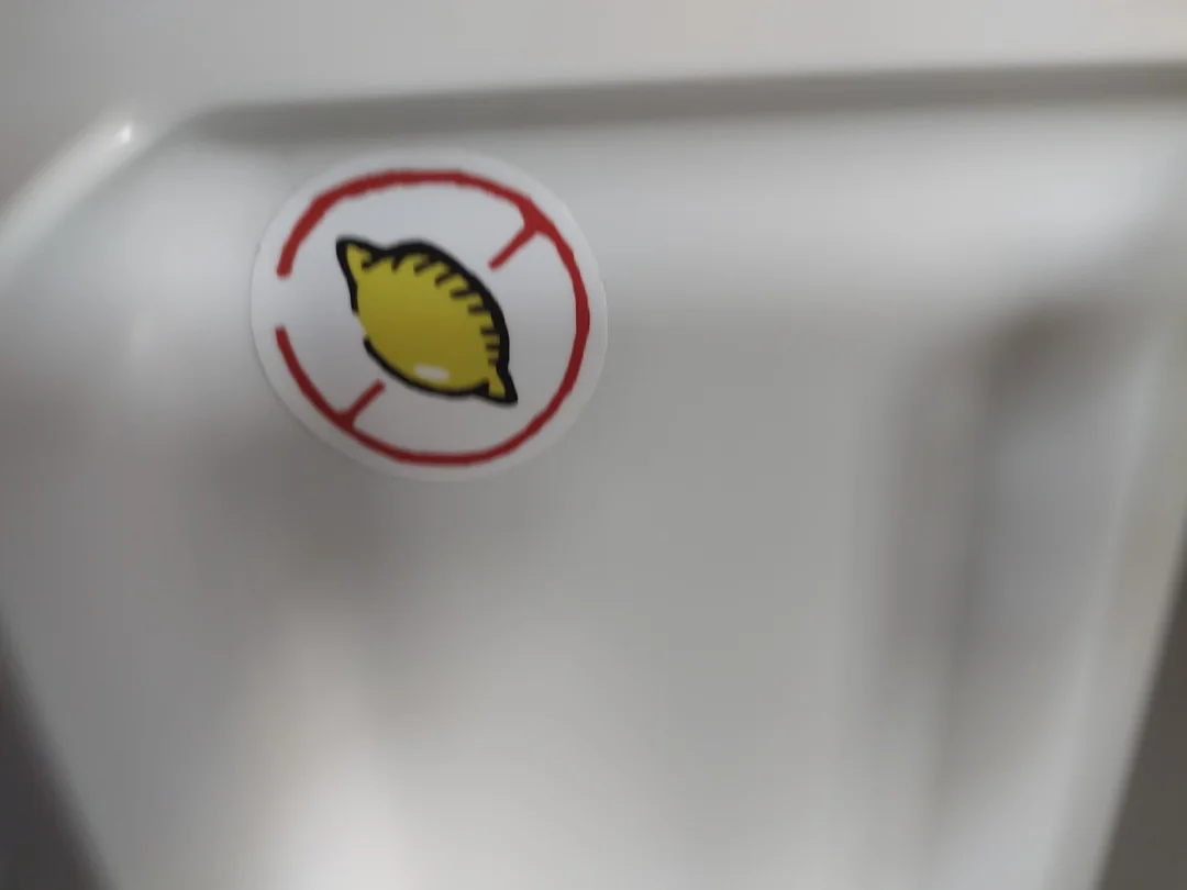 Nálepka citróna v červenom kruhu na bielom pozadí, symbol zákaz používania citrusov.