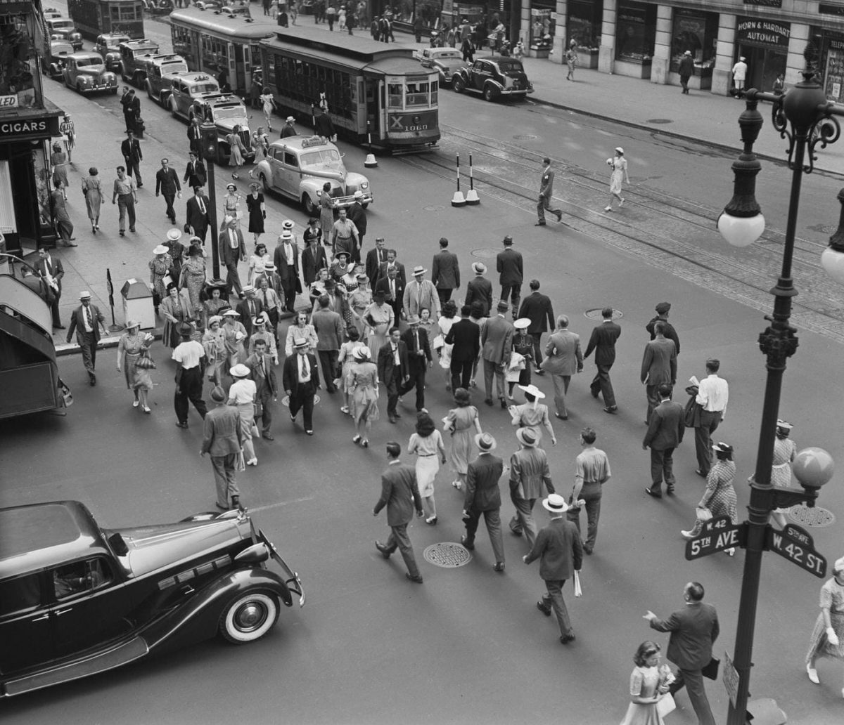 Historická fotografia prechodu na rušnom veľkomestskom námestí s autami, električkou a početnou množinou chodcov.