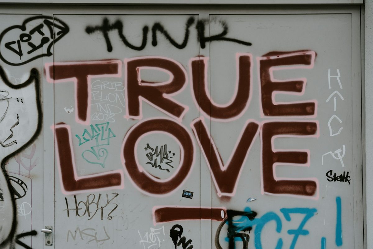 Graffiti na stene s textom TRUE LOVE v červenej farbe, obklopené rôznymi kresbami a podpismi sprejom.