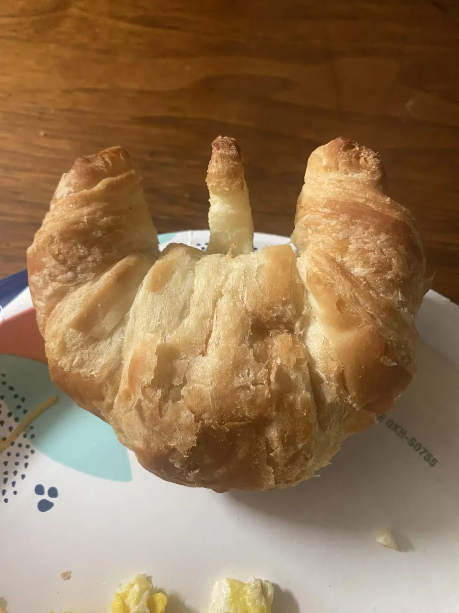 Croissant na tanieri pripomínajúci tvar rúk, detail kuchynského stola na pozadí.