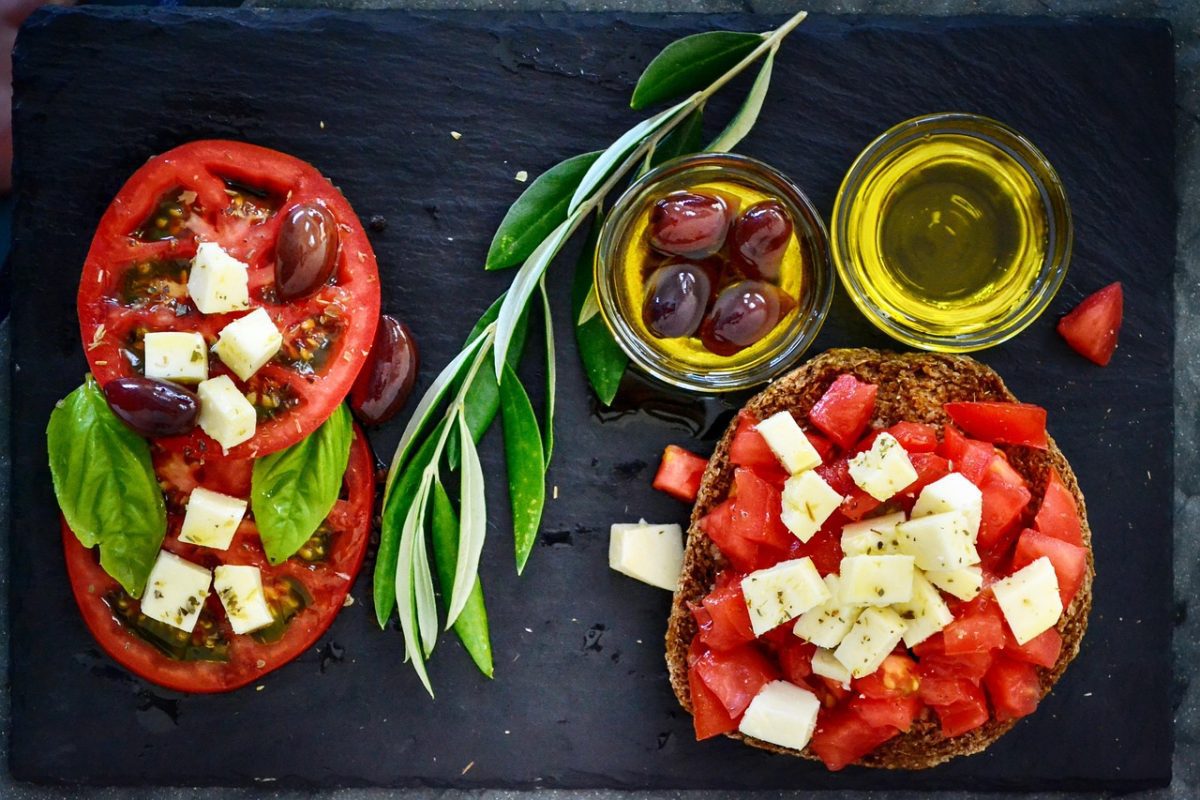Chutná talianska bruschetta s paradajkami, syrom, olivami, bazalkou a olivovým olejom na tmavej doske, zdobená olivovou vetvičkou.