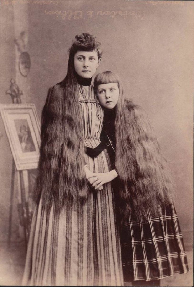 Dve ženy v historickom odeve s dlhými vlasmi, viktoriánska éra, stará fotografia.