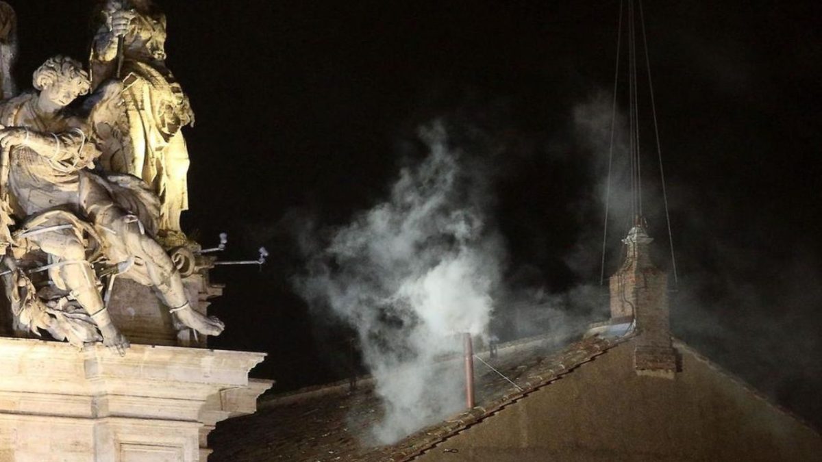 Biela dymová signalizácia na komíne a sochy na streche v noci.