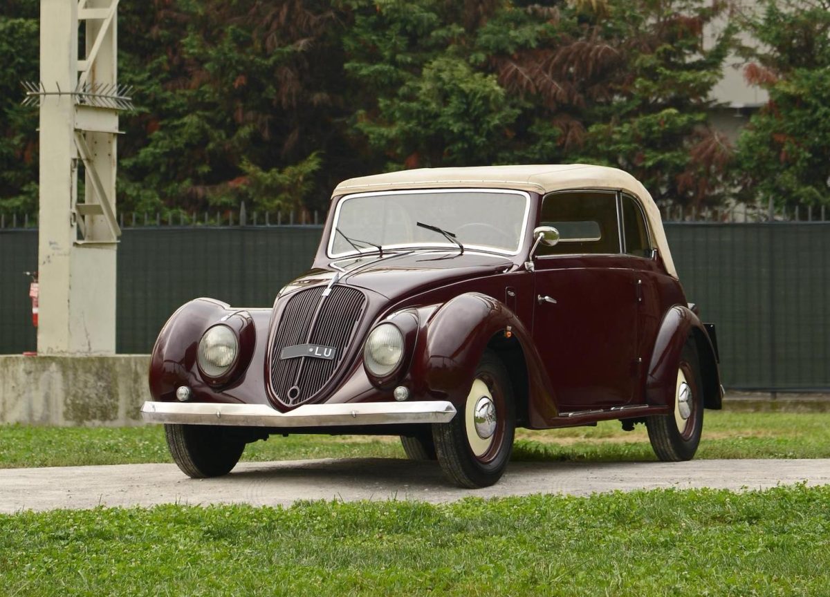 Historické vínové kabriolet auto z 30. rokov na trávniku, s lesklou karosériou a bielou strechou.