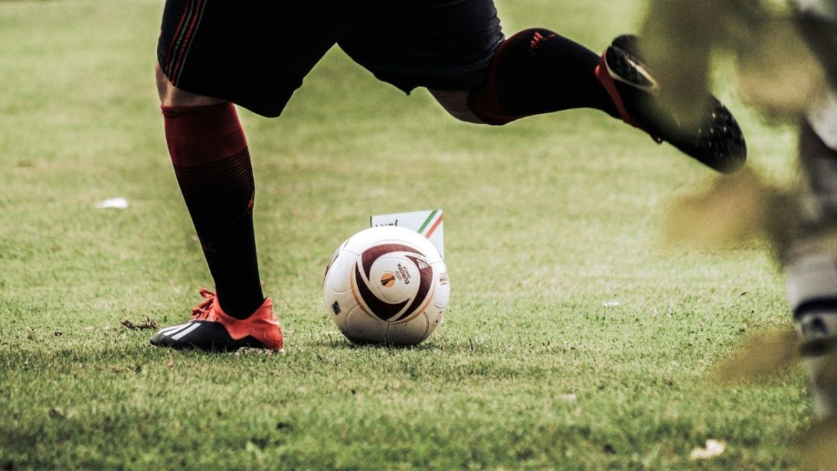 Futbalista pripravujúci sa na kop pri rohovom kope, futbalová lopta na trávniku.