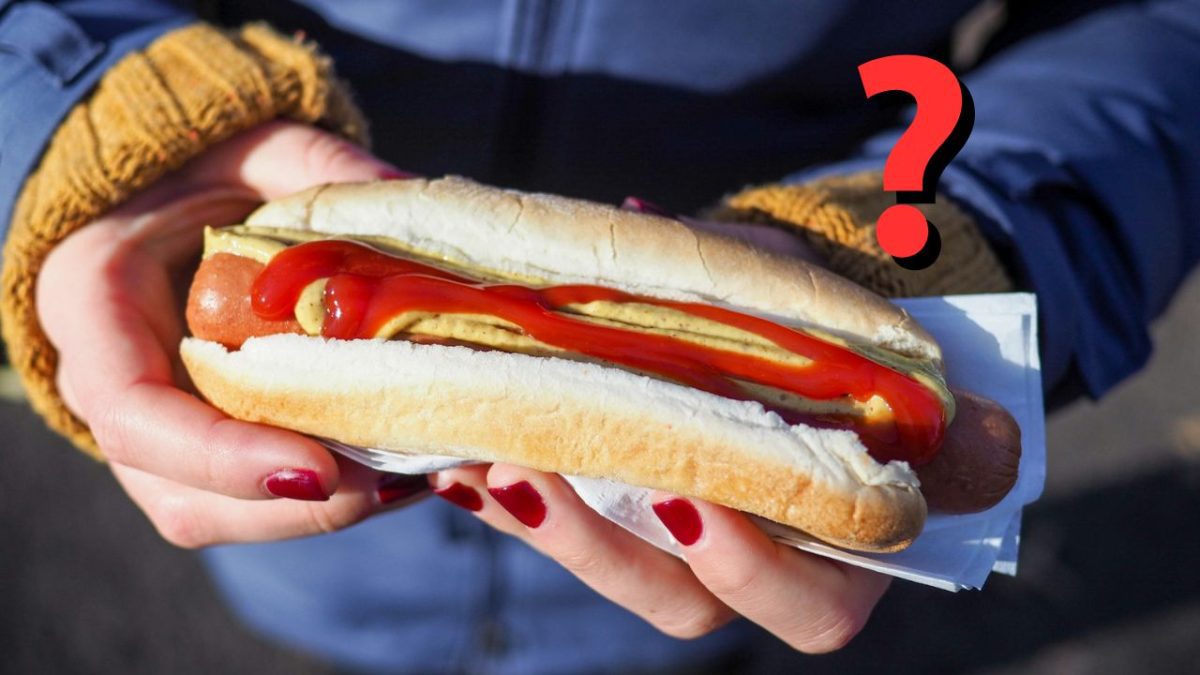 Osoba drží hotdog s horčicou a kečupom. V otázke, koľko toho vieš o hotdogo?