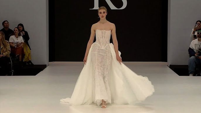 Modelka predvádzajúca elegantné biele svadobné šaty na módnej prehliadke, výrazný moderný dizajn.