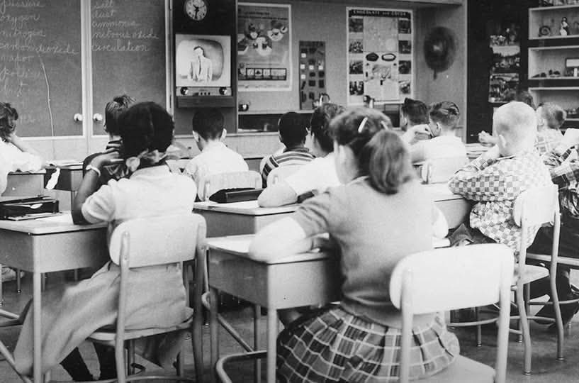 Deti v školskej triede sledujú televízor, klasická vyučovacia scéna z obdobia minulého storočia.