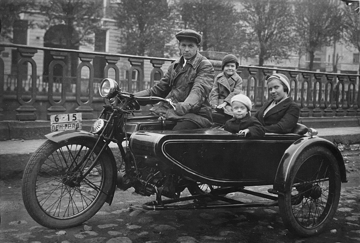 Rodina na historickom motocykli s postranným vozíkom, jazdiaci po kamennej dlážke mesta.